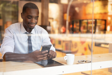 Businessman drinking coffee in cafe. Handsome African man using the phone