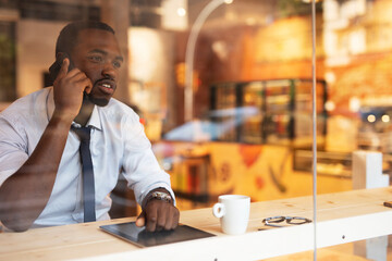 Businessman drinking coffee in cafe. Handsome African man talking to the phone while enjoying in fresh coffee..