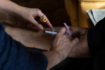 Middle-aged home nurse making a blood transfusion to an elderly patient for a blood test.