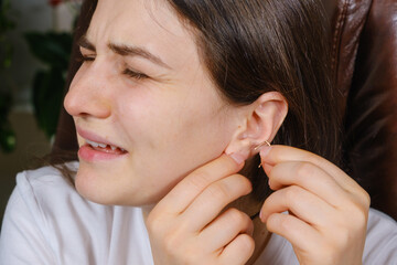 A woman tries to put an earring in her ear, earlobe problem, the hole is overgrown
