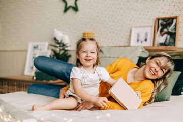 Mom and daughter read fairy tales in the bedroom on the bed on Christmas or New Year's Eve. Holiday atmosphere, Christmas mood