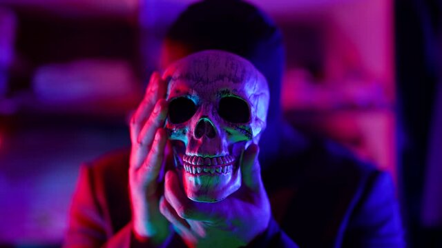 serial killer and maniac with human skull in hands, gloomy man with black mask on head