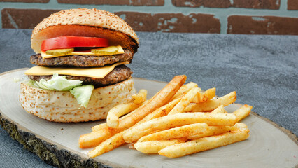 Double juicy cheeseburger with french fries, lettuce, tomato, cheddar cheese front of vintage brick wall