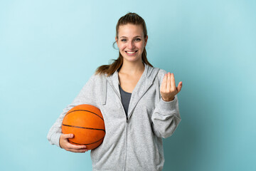 Young caucasian woman isolated on blue background playing basketball and doing coming gesture