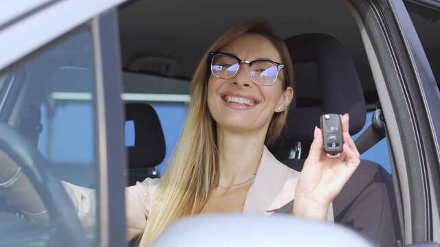 Excited young woman holding key from auto in hand, happy with car purchase