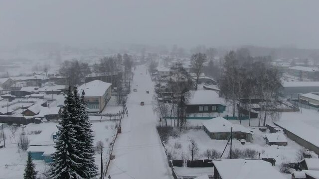 Aerial shot in movement over road to the right of snowed town when strong snow-storm in evening