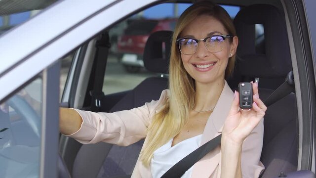 Happy young female sitting in auto, showing car key and smiling, rental service