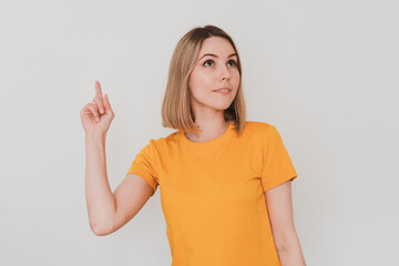 Fototapeta premium young woman in yellow t-shirt pointing her finger up. On white background. Hand gestures