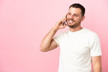 Young Brazilian man isolated on pink background keeping a conversation with the mobile phone