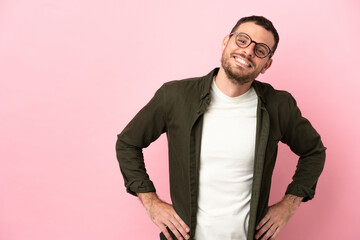Fototapeta premium Young Brazilian man isolated on pink background posing with arms at hip and smiling