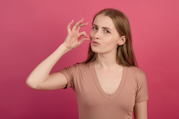 Fototapeta premium Portrait of young and attractive Caucasian blonde girl showing smoker gesture with cigarette on pink studio background.