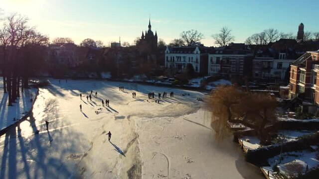 Ice skating people on a frozen canal in the city center of Zwolle during a beautiful winter day in Overijssel, The Netherlands. Aerial drone point of view.