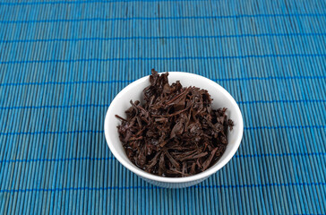 Tea leaves after brewing in a white bowl on a blue mat.