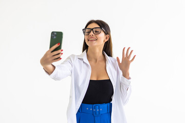 Young woman taking selfie, sending kisses at mobile phone camera, romatnic video call on smarpthone app, standing against white background