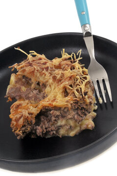 Portion de hachis parmentier dans une assiette avec une fourchette en gros plan sur fond blanc