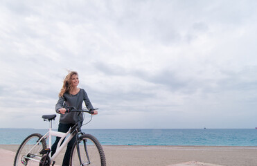 Fototapeta premium Beautiful young woman walking near the sea with bicycle against sky background.