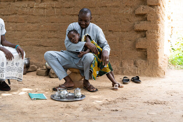 Loving black father playing with his daughter in the courtyard of his traditional mud house in West Africa