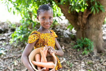 Beautiful young black african girl with some giant carrots in her pumpkin bowl on her way to the...