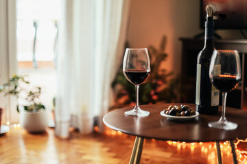 Two glasses of red wine on a wooden table at home, Christmas lights 
