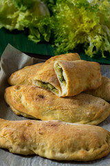 Panzerotti with escarole and grana padano baked in the oven with parchment paper. Close-up of panzerotti on green wood background and smooth and curly endive tufts in the background