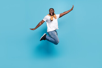Photo of carefree guy jump raise hands enjoy flight wear t-shirt jumper front-tie isolated blue color background