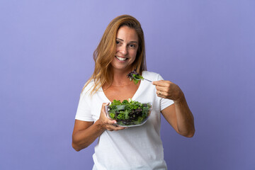 Middle age brazilian woman isolated on purple background holding a bowl of salad with happy expression