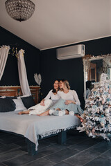 Two young women sitting on the bed next to christmass tree