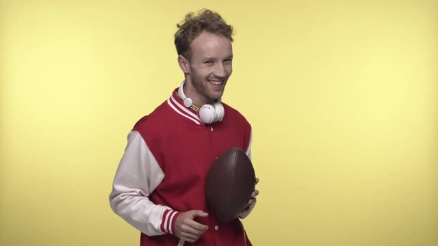 young man in bomber jacket holding rugby ball on yellow
