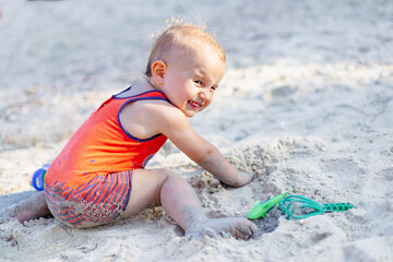 Little toddler boy playing with sand on a beach. Child wearing sun protection clothes. Summer vacation in France. Holidays with children concept, copy space.