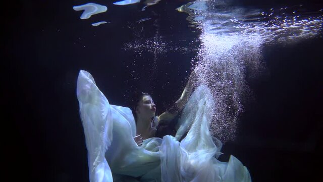 A girl is dancing underwater in a pool equipped for shooting videos and photos. A young girl demonstrates movements in slow motion