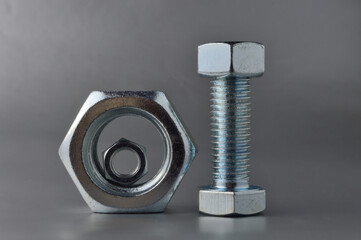 composition of new bolts and nuts of different sizes on a gray background.