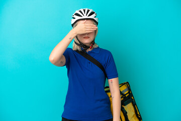 Young caucasian woman with thermal backpack isolated on blue background covering eyes by hands. Do not want to see something