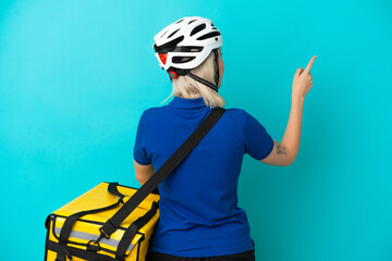 Young caucasian woman with thermal backpack isolated on blue background pointing back with the index finger