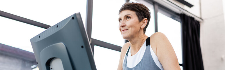 Fototapeta na wymiar Low angle view of elderly sportswoman training in treadmill in gym, banner.