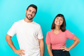Obraz premium Young couple isolated on blue background posing with arms at hip and smiling