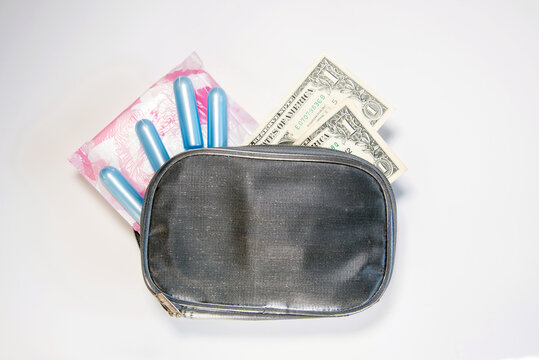Productos de higiene femenina como toallas sanitarias y tampones que salen de un neceser gris junto a dos billetes de d&oacute;lar. Concepto del costo de los productos menstruales