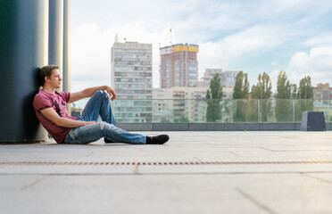 Fototapeta na wymiar Handsome and relaxed. Young man in casual wear sitting on the floor outdoors.