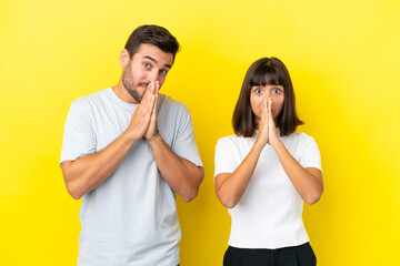 Young couple isolated on yellow background keeps palm together. Person asks for something