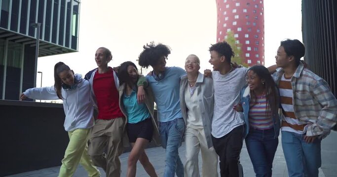 Multiethnic group of young happy friends walking and jumping down the street holding each other affectionately.