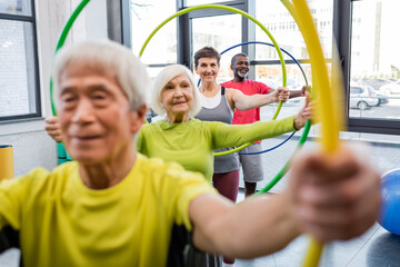 Smiling woman in sportswear training with hula hoop near multiethnic friends in sports center.
