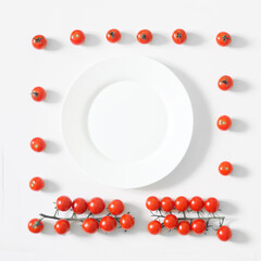 Red cherry tomatoes on a white kitchen table next to a round white plate. Square. Shades of white and red