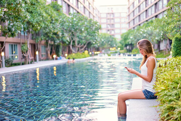 Summer and technology. Pretty young woman using smart phone at swiming pool.