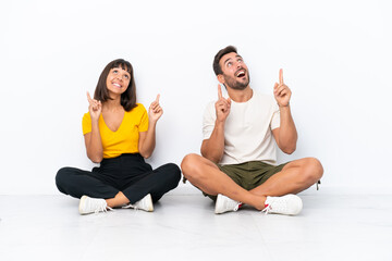 Fototapeta na wymiar Young couple sitting on the floor isolated on white background pointing with the index finger a great idea