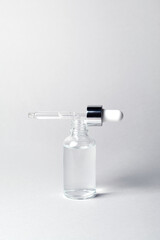 Fototapeta na wymiar Open glass bottle with silver and white pipette on grey background mockup. Transparent facial serum in dropper closeup. Cosmetic product for advertising. Minimal concept. Vertical photo, copy space.