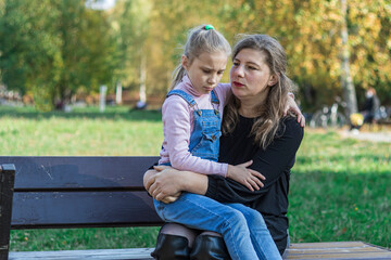 outdoors. mom is sitting on a bench and holding a baby in her arms. sunny day