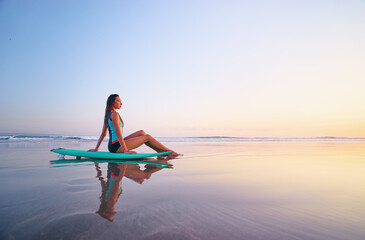 Surfing and vacation. Holiday on the beach. Relaxed young woman sitting on the sand with surf board...