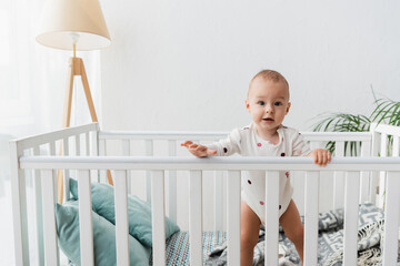 toddler boy looking at camera while standing in crib.