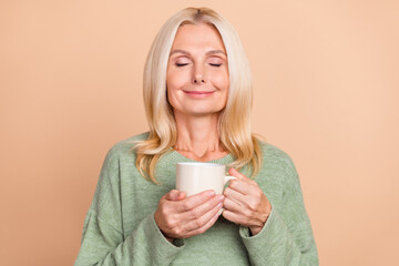 Photo of cute dreamy lady pensioner dressed green pullover enjoying tasty cacao isolated beige...
