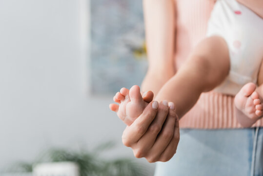 cropped view of woman touching tiny foot of son on blurred background.