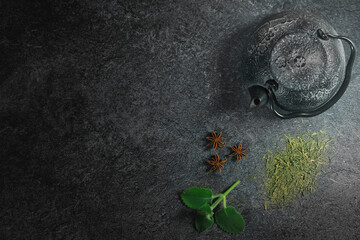 Top studio shot of a still life with vintage black metal Japanese tea pot on a dark stone table. Free copy space for caption. Tea ceremony concept. Hot beverage preparation. Green tea and anise star.